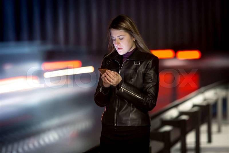Portrait of woman with mobile phone walking at night next to highway, stock photo