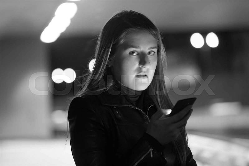 Closeup black and white portrait of lonely woman posing on dark street with telephone, stock photo