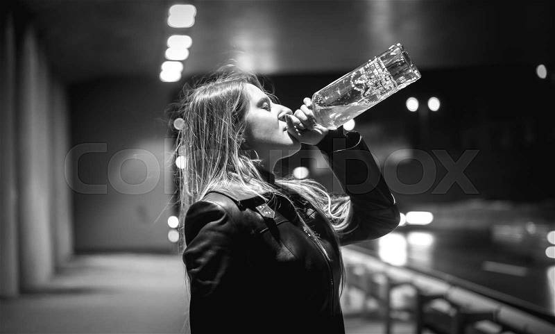 Closeup black and white portrait of woman drinking whiskey at night on street, stock photo