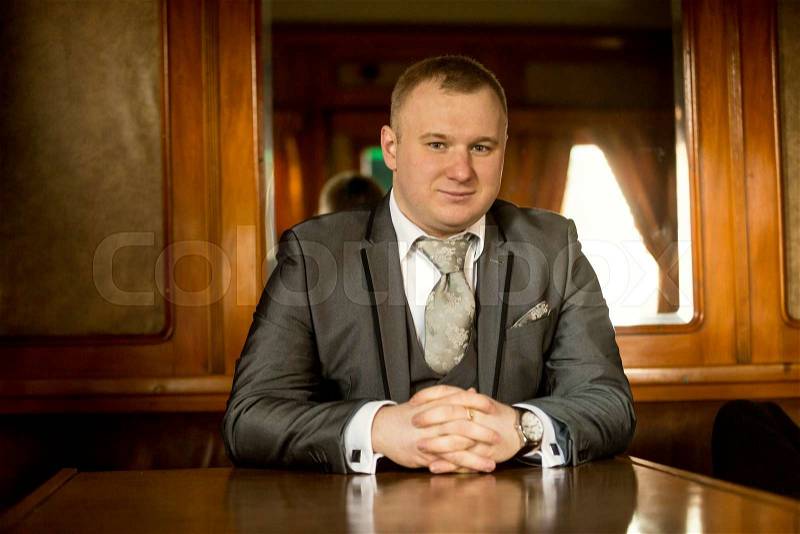 Portrait of man in suit sitting at old wooden table, stock photo