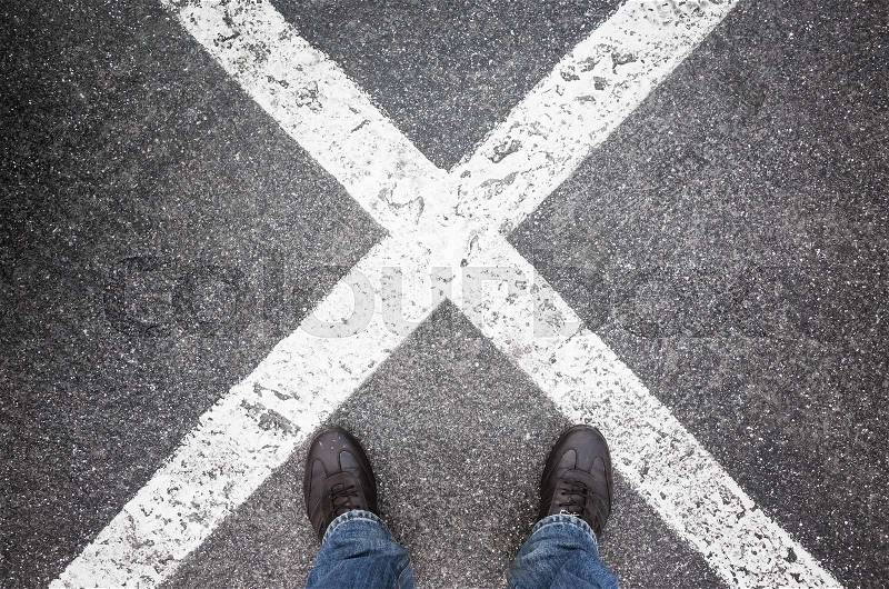 Male feet standing on dark urban asphalt with crossing lines of road marking, stock photo