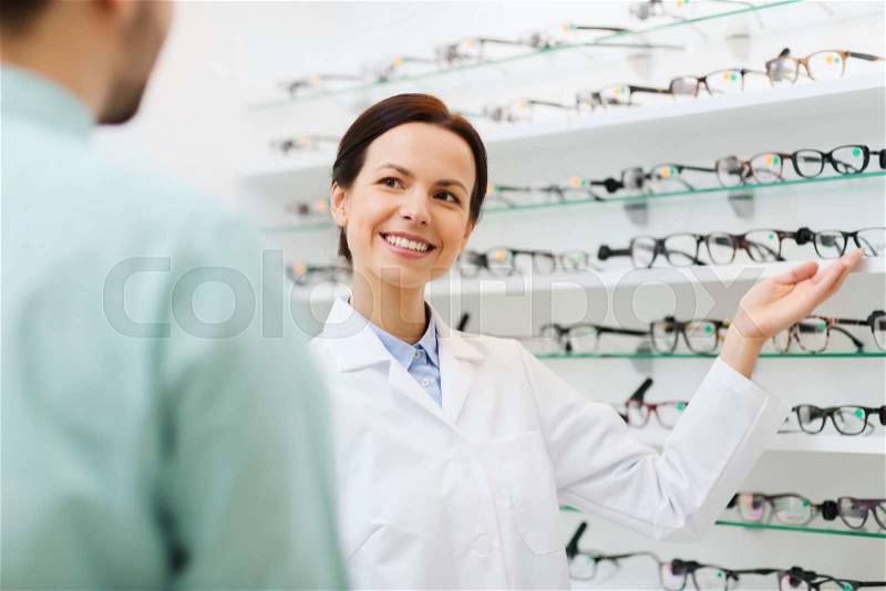 Health care, people, eyesight and vision concept - female optician showing glasses to man at optics store, stock photo