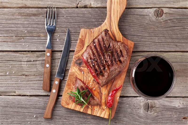 Grilled beef steak with rosemary, salt and pepper and wine on wooden table. Top view, stock photo