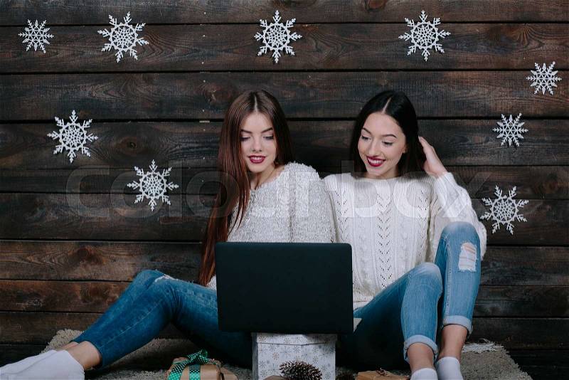 Two beautiful girls siting on the floor with a laptop, between gifts for Christmas, stock photo