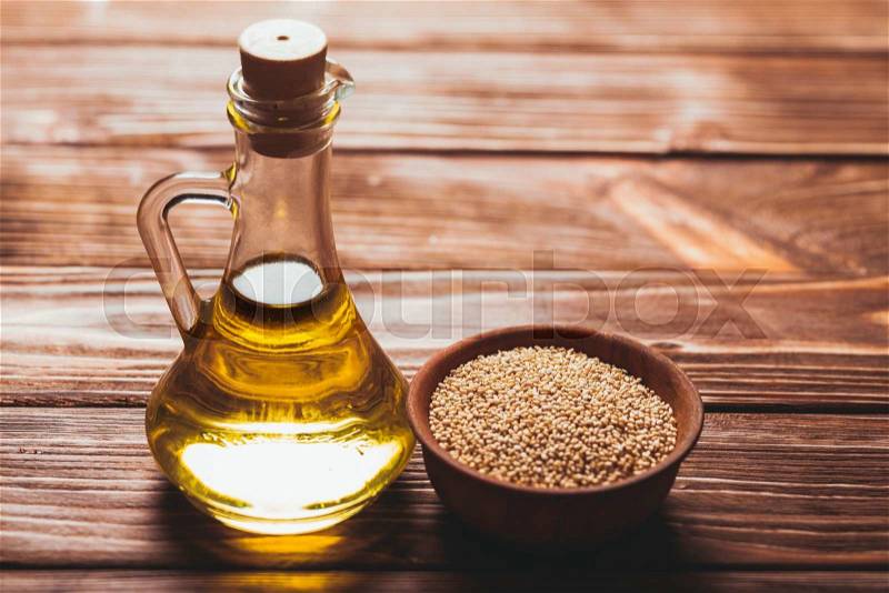 Sesame oil in a glass bottle with a cork and heap sesame seeds in a wooden bowl, stock photo