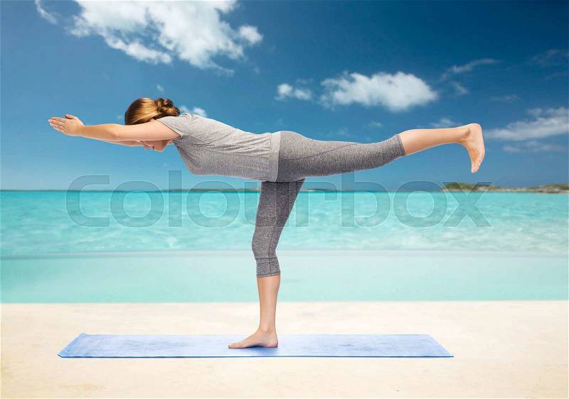Fitness, sport, people and healthy lifestyle concept - woman making yoga warrior pose on mat over beach background, stock photo