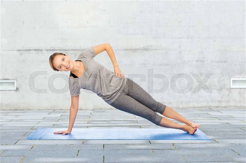 Fitness, sport, people and healthy lifestyle concept - woman making yoga in side plank pose on mat over urban street background, stock photo