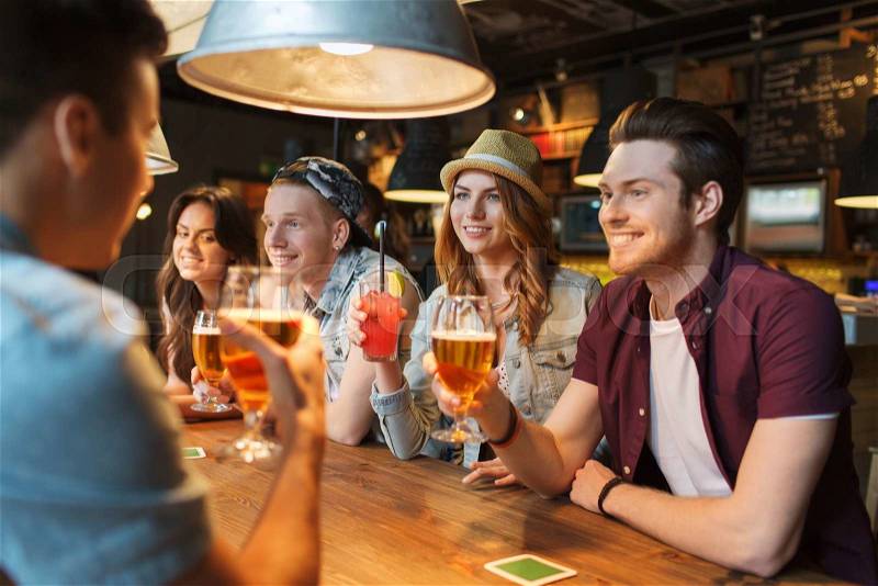 People, leisure, friendship and communication concept - group of happy smiling friends drinking beer and cocktails talking at bar or pub, stock photo