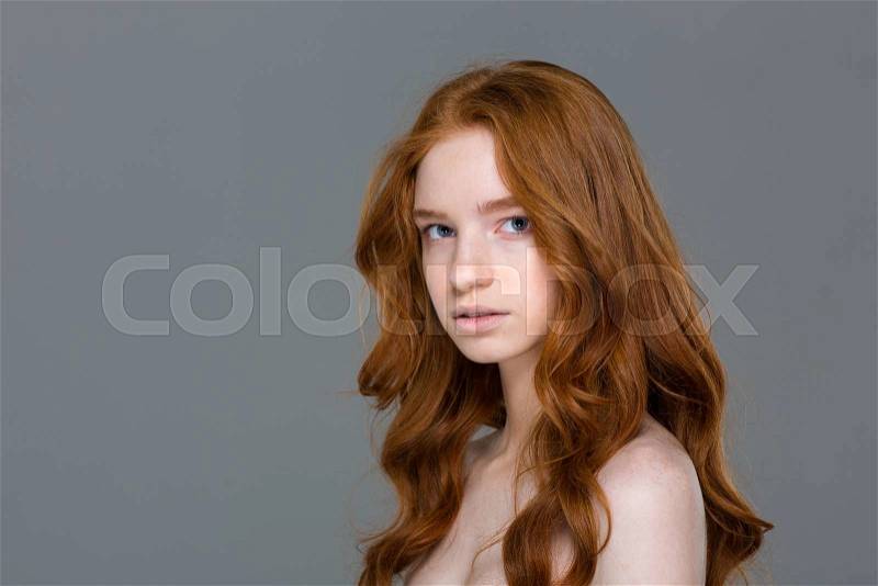 Beauty portrait of a young redhead woman looking at camera on gray background, stock photo