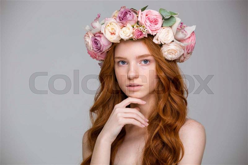 Beautiful redhead young female with curly red hair in flower wreath over grey background, stock photo