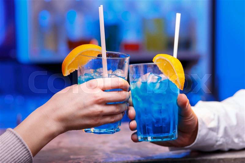 The hands with alcohol cocktails making toast on a blue bar background, stock photo