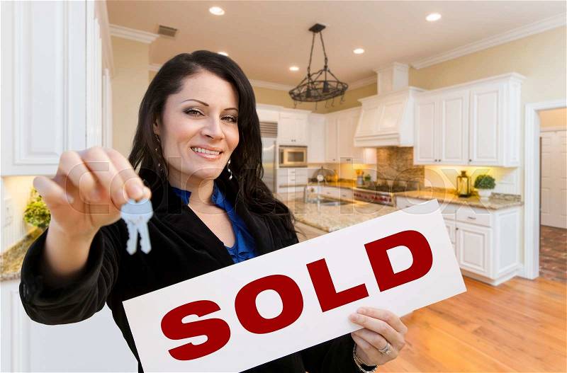 Pretty Hispanic Woman In Kitchen Holding House Keys and Sold Sign, stock photo