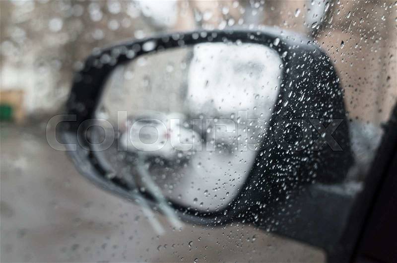 Wet car window with raindrops and mirror behind. Close-up photo with selective focus and shallow DOF, stock photo