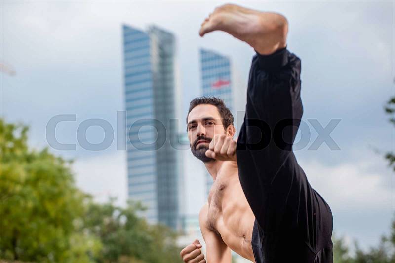 Sportsman doing karate kick in city downtown, stock photo