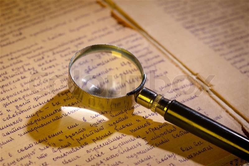 Magnifier glass on page of ancient manuscript, old newspaper. Small depth of field, stock photo