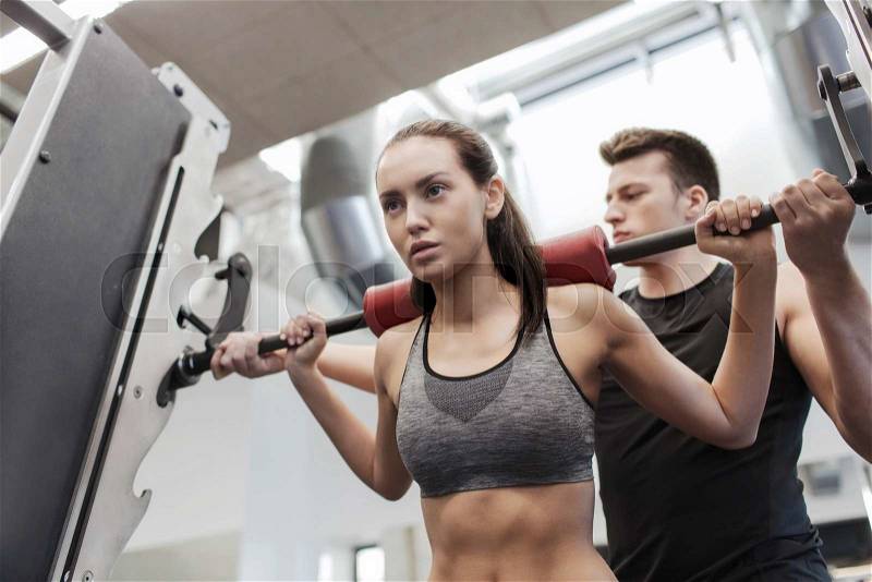 Sport, fitness, teamwork, weightlifting and people concept - young woman and personal trainer with barbell flexing muscles in gym, stock photo