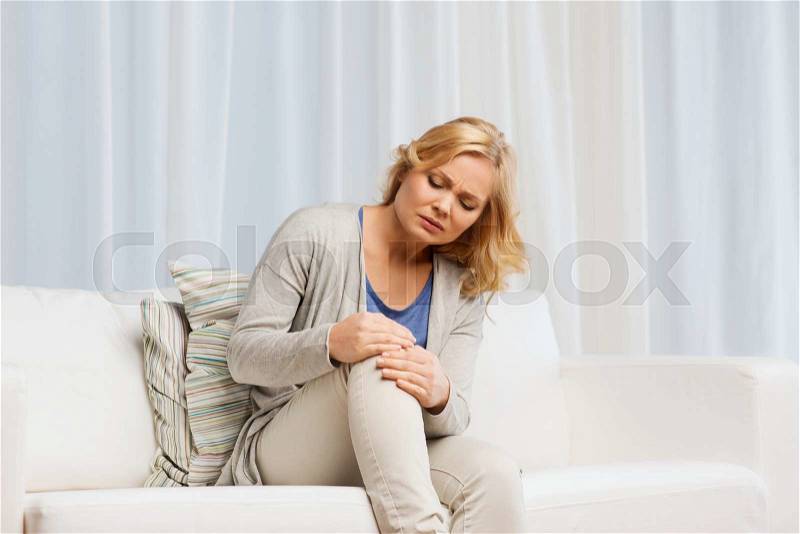 People, healthcare and problem concept - unhappy woman suffering from pain in leg at home, stock photo