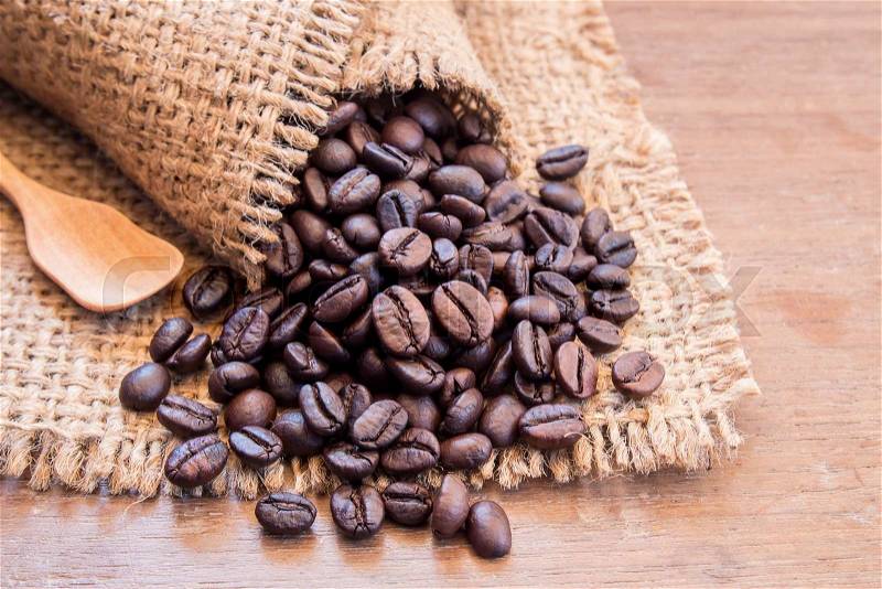 Black coffee beans in burlap sack on wooden table, selective focus, stock photo