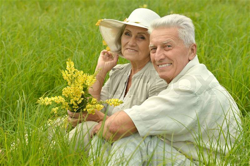 Beautiful senior couple in summer field with flowers, stock photo