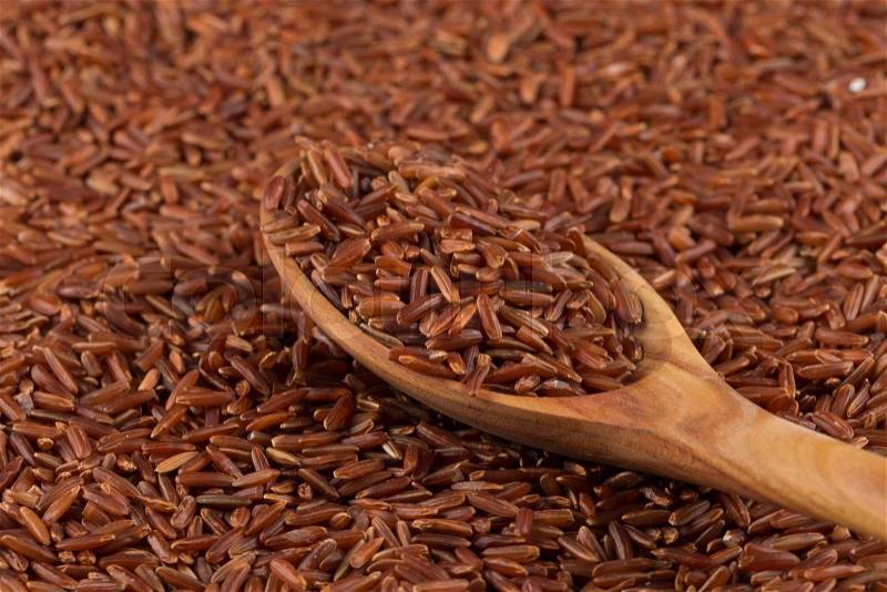 Red rice in a wooden spoon on red rice background, stock photo