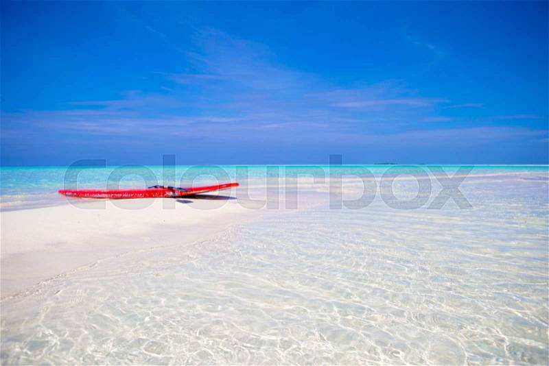 Red surfboard on white sandy beach with turquoise water at tropical island in Indian Ocean, stock photo
