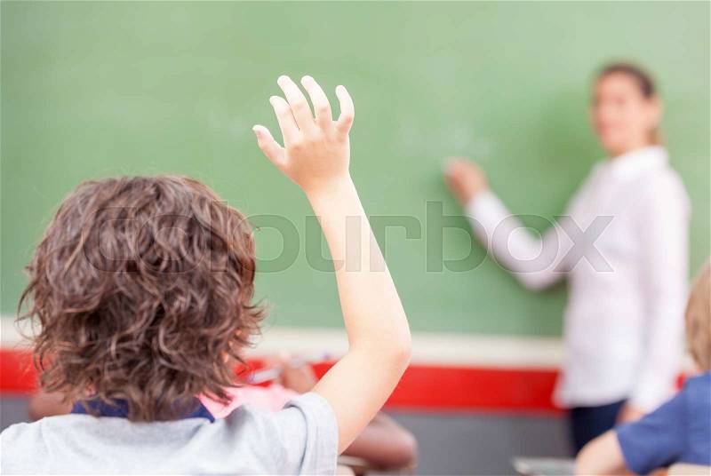 Raising hand at class lesson, primary school scene. Success and education concept, stock photo