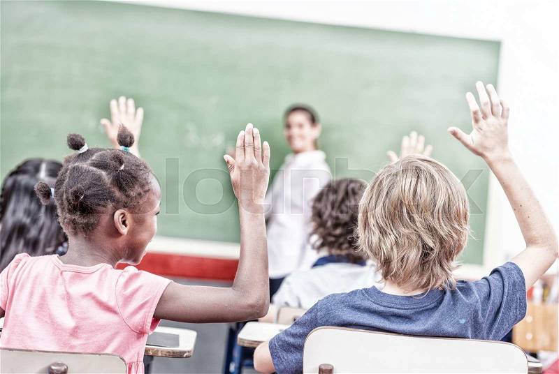 Raising hand at class lesson, primary school scene. Success and education concept, stock photo