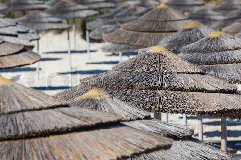 Detail of woven umbrellas above rows of many relaxing beds and loungers on beach , stock photo