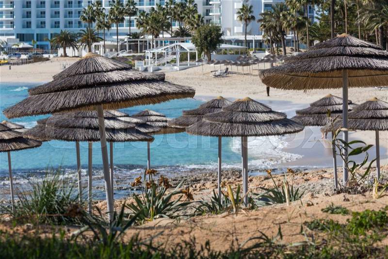 Detail of woven umbrellas above rows of many relaxing beds and loungers on beach , stock photo