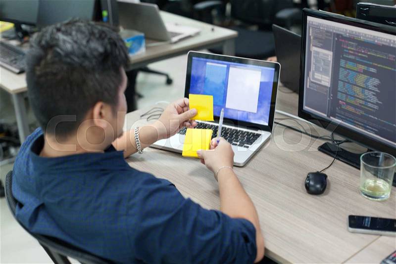 Asian business man yellow sticky note, rear back view thinking idea computer developer working desk laptop sitting real office, stock photo