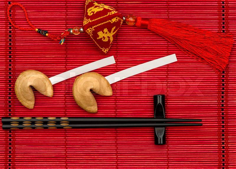 Chinese new years lucky charm, fortune cookies and black chopsticks on red bamboo mat, stock photo