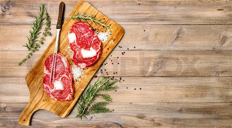 Rib Eye Steak with herbs and spices on wooden kitchen desk. Raw beef meat. Food background, stock photo