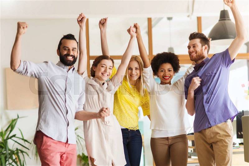 Business, triumph, gesture, people and teamwork concept - happy international creative team raising hands up and celebrating victory in office, stock photo