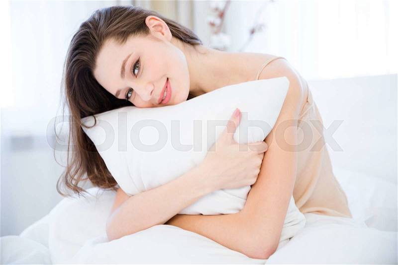 Happy beautiful relaxed young woman hugging pillow on bed in bedroom , stock photo
