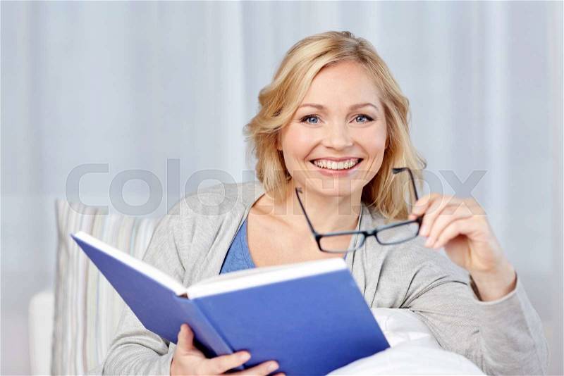 Leisure, literature and people concept - smiling middle aged woman reading book and sitting on couch at home, stock photo