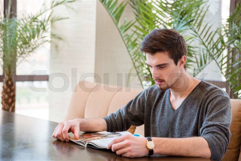 Portrait of a young man reading magazine in restaurant, stock photo