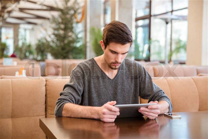 Portrait of a young man sitting at the table and using tablet computer in restaurant, stock photo