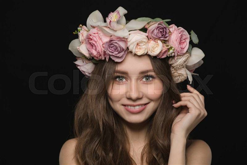 Portrait of a happy woman with wreath from flowers on head looking at camera over black background, stock photo