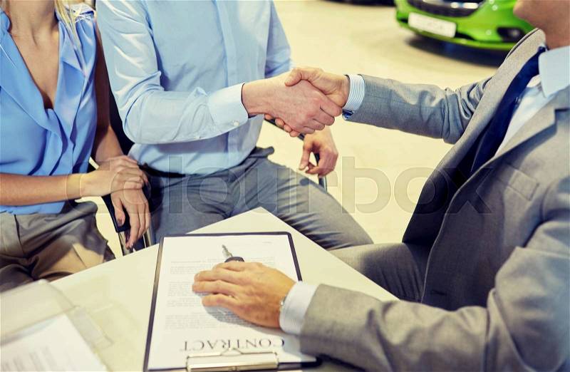 Auto business, car sale, gesture and people concept - close up of customers couple with dealer shaking hands in auto show or salon, stock photo