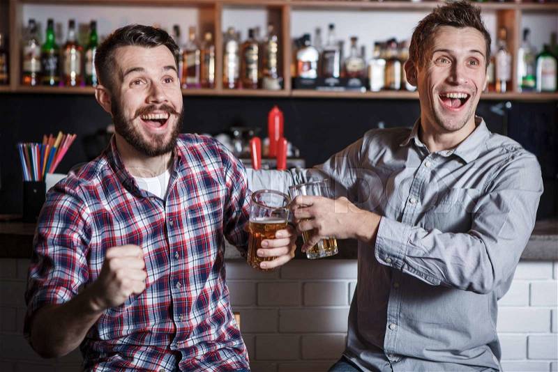 Young fun people with beer watching football in a bar, stock photo
