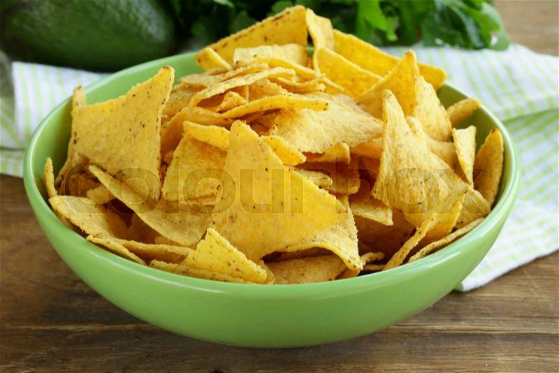 Corn chips (nachos) in a green bowl on wooden table, stock photo