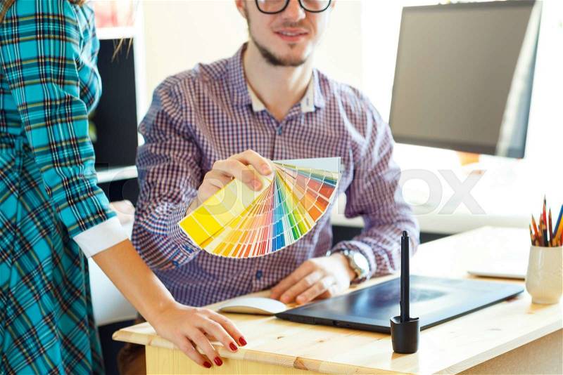 Young colleague - manand woman looking to a color paint palette at home office, modern business concept, stock photo