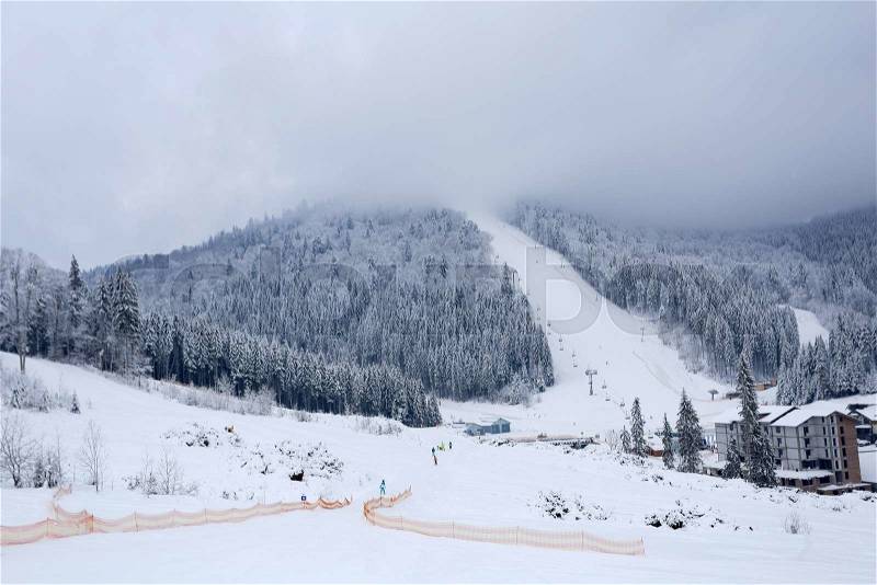Landscape winter ski slopes in sport village. Snow-covered trees, small houses and ski lifts. Mountain in a fog, stock photo