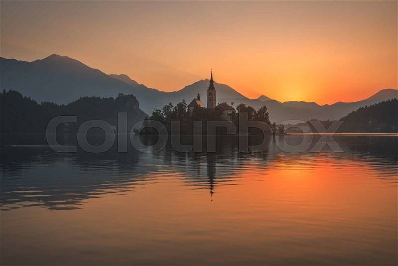 Little Island with Catholic Church in Bled Lake, Slovenia at Beautiful Colorful Sunrise with Castle and Mountains in Background, stock photo
