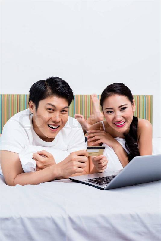 Chinese couple shopping online from their bedroom, stock photo