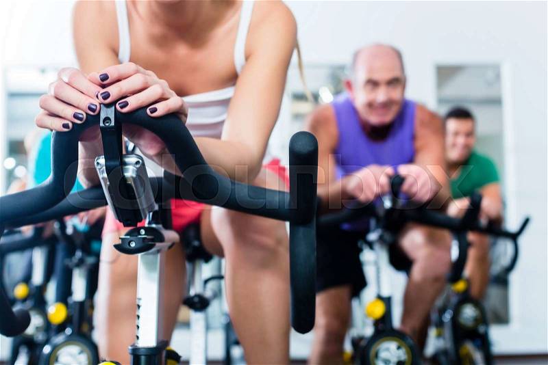 Group Senior and young people in spinning course on fitness bike in gym doing endurance and cardio training, the instructor is leading them on, stock photo