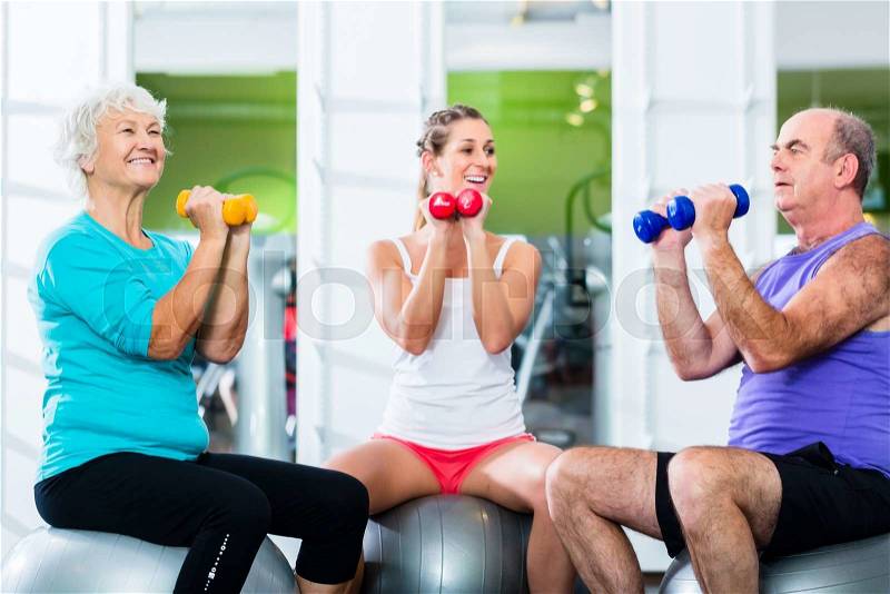 Senior man and women with fitness trainer in gym lifting barbells as sport exercise, stock photo