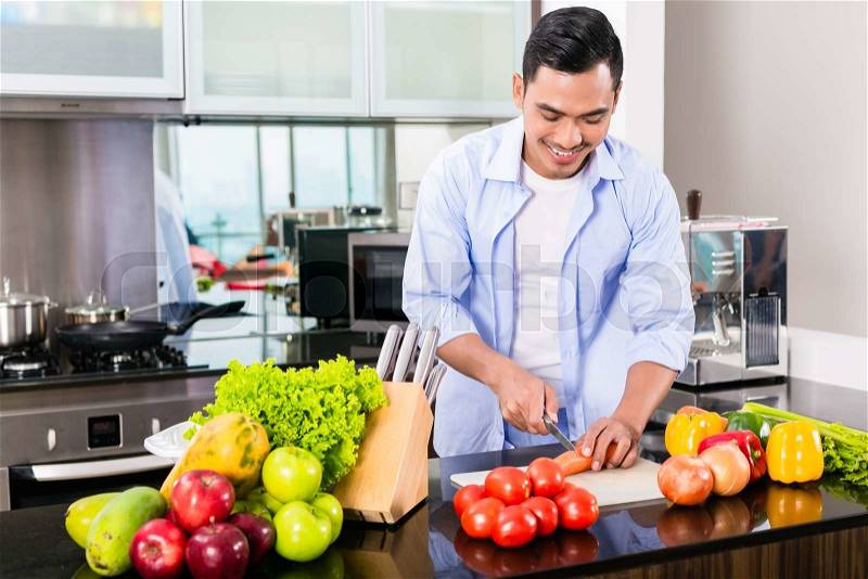 Asian man cutting vegetables in domestic kitchen preparing salad, stock photo