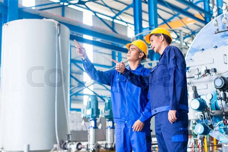 Worker in Asian manufacturing plant discussing in front of machines, stock photo