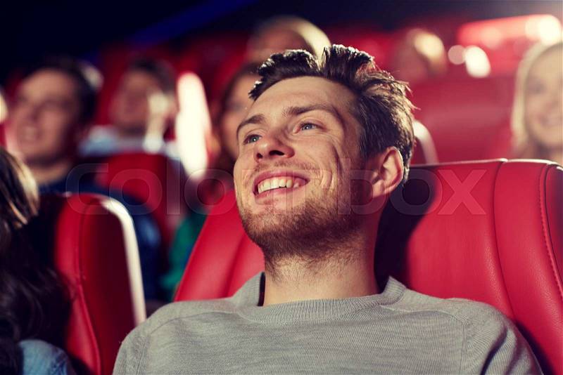 Cinema, entertainment and people concept - happy young man watching comedy movie in theater, stock photo